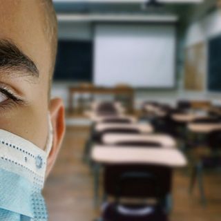 scuola con banchi e ragazzo in primo piano con la mascherina