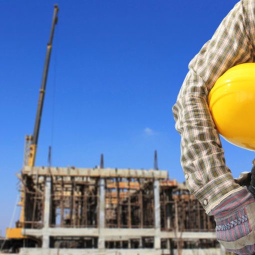 muratore con caschetto sotto il braccio e cantiere sullo sfondo