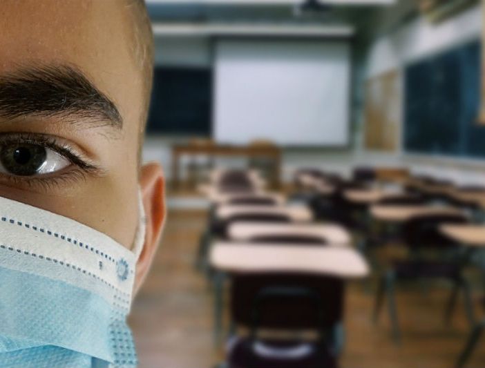 scuola con banchi e ragazzo in primo piano con la mascherina